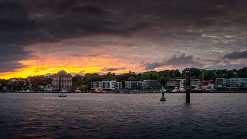 Scenic view of river by buildings against dramatic sky