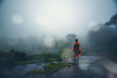 Rear view of man standing on road during rainy season