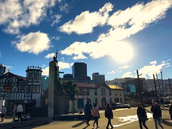 People walking on street amidst buildings in city against sky