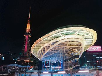 Illuminated ferris wheel in city against sky at night