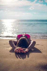 Woman sitting on shore at beach against sky