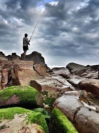 Boy standing on rock against sky