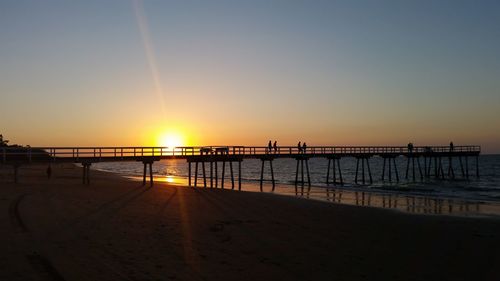 Silhouette pier on beach against clear sky during sunset