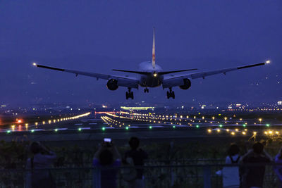 Airplane flying at airport runway against sky at night