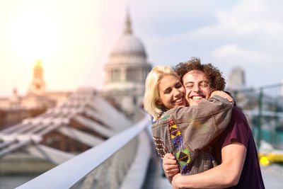 Side view of happy young couple embracing while standing against sky in city
