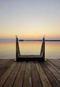 Wooden jetty in sea against sky during sunset