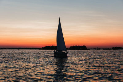 Silhouette sailboat sailing on sea against sky during sunset