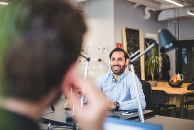 Businessman smiling while looking at male colleague in office