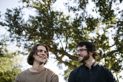 Low angle view of brothers talking while sitting against trees at park