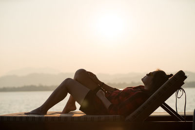 Side view of young woman relaxing in swimming pool against sky