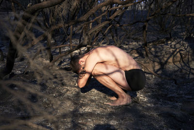 Shirtless man crouching on forest floor