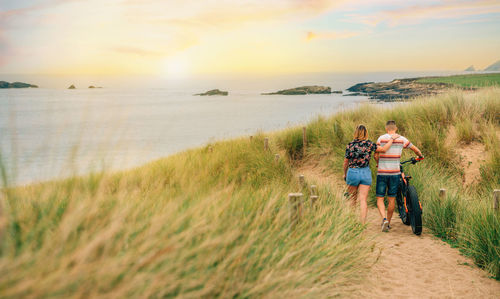 Rear view of woman walking on beach against sky during sunset