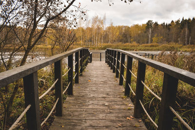 Footbridge amidst trees in forest against sky