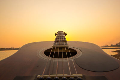 Close-up of guitar against sky during sunset