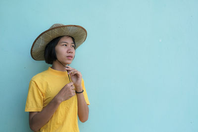 Young woman looking away while standing against blue wall