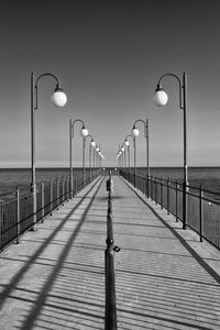 Street lights on pier by sea against sky