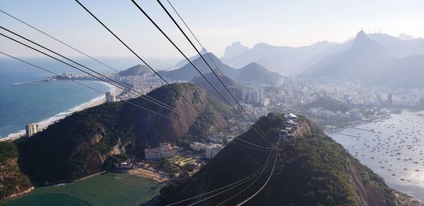 Overhead cable car over sea and mountains against sky