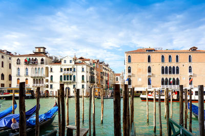 Gondolas moored at canal by buildings against cloudy sky