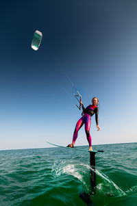 Full length of woman surfing in sea against clear sky