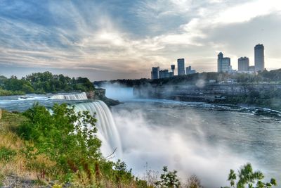 Scenic view of waterfall in city against sky