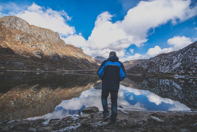 Rear view of mature man standing at lakeshore against cloudy sky