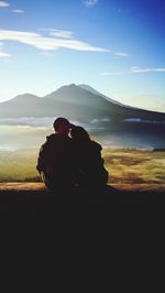 Rear view of silhouette of couple sitting by mountain against sky