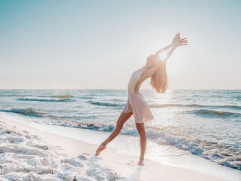 Woman dancing with arms raised on beach against clear sky