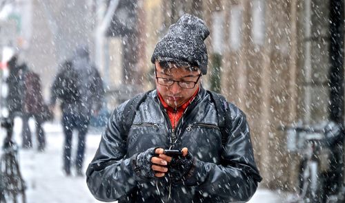 Woman holding smart phone while standing on snow