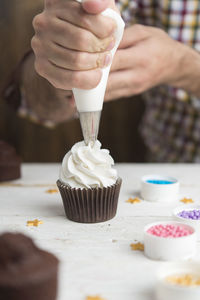 Midsection of man icing on cupcake at table