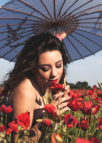 Young woman with umbrella smelling red flowers during sunny day