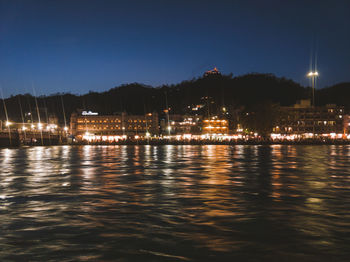 Illuminated city by river against clear sky at night