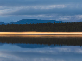 A tranquil dawn illuminates a lake in norway, its reflection shimmering beneath the morning mist. 