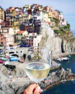 Cropped hand of person holding alcoholic drink against townscape