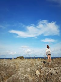 Rear view of person standing next to sea against cloudy sky