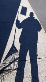Shadow of man with gardening fork on road during sunny day