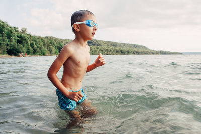 Shirtless boy standing in sea against sky