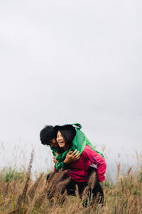 Happy woman piggybacking man at field against clear sky