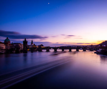 Bridge over river in city against sky at sunset