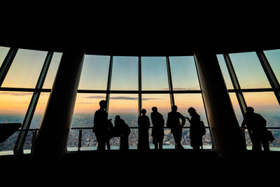 Silhouette people looking through window at sunset
