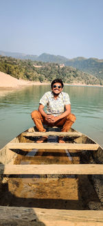 Portrait of man sitting by lake against mountain