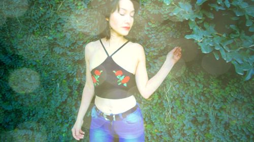 Young woman looking away while standing against plants