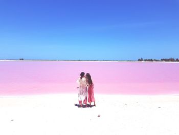 Rear view of woman with pink umbrella against blue sky