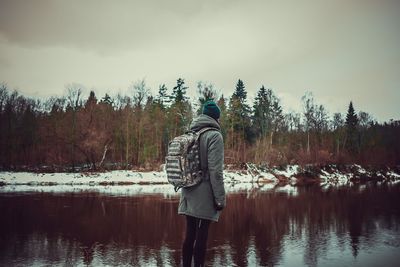 Rear view of man standing by lake against sky