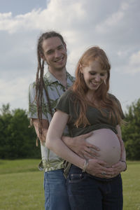 Portrait of man holding pregnant woman abdomen on field