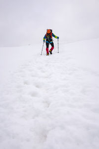 Male hiker climbing snowcapped mountain with hiking poles