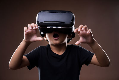 Boy using virtual reality simulator while standing against brown background