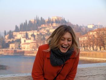 Laughing woman standing by lake against sky 