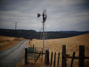 American-style windmill on grassy field against cloudy sky