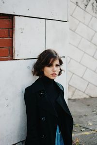 Young woman looking down while standing against wall