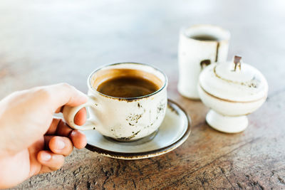 Cropped hand holding fresh espresso cup on table
